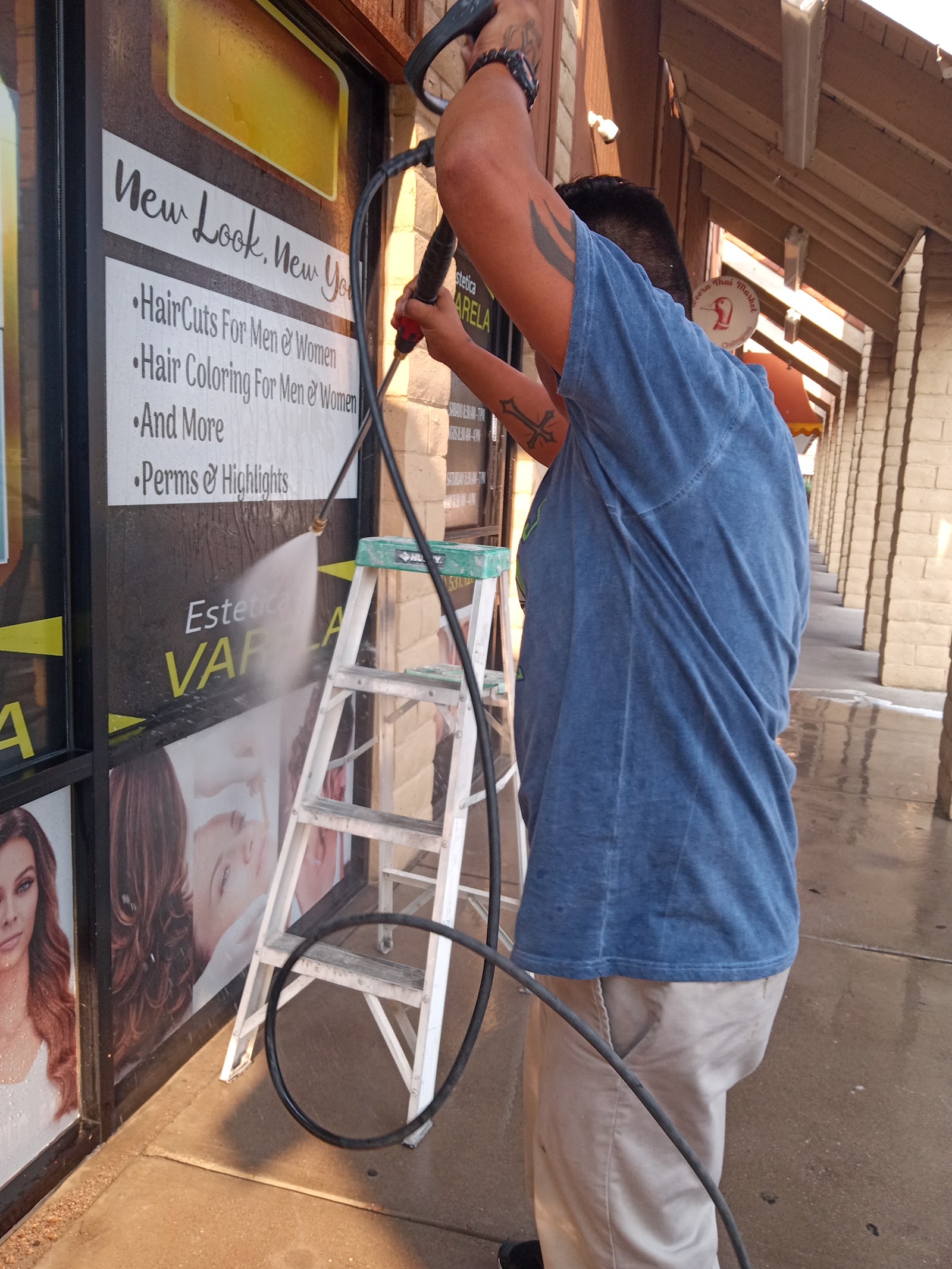 Worker pressure washing a storefront window and signage at a strip mall