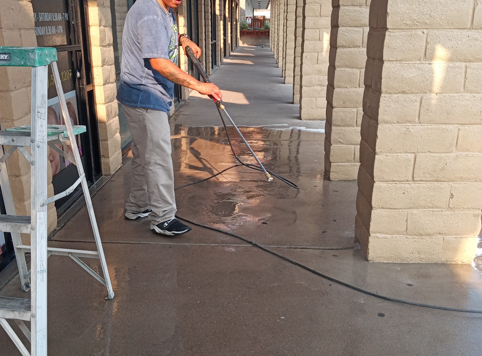 Worker pressure washing a wet concrete walkway at a strip mall