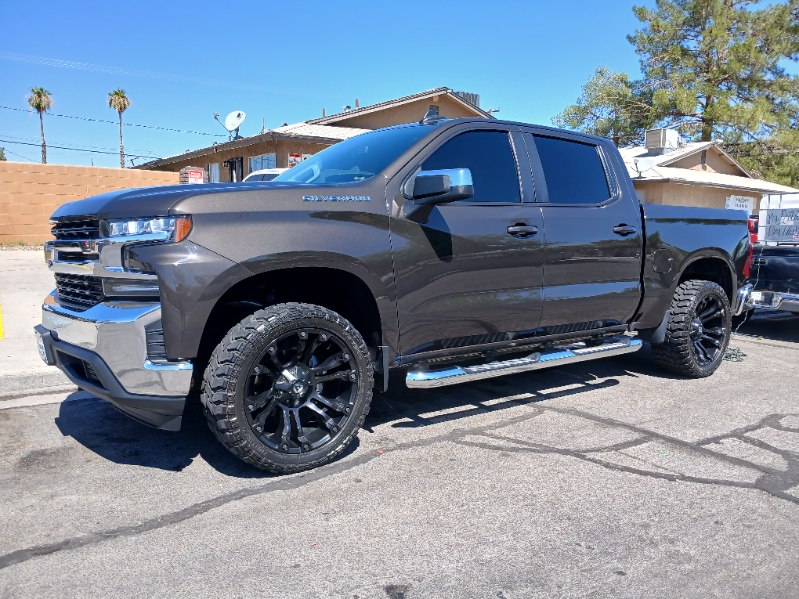 Clean lifted gray Chevy Silverado with black wheels parked under a blue sky